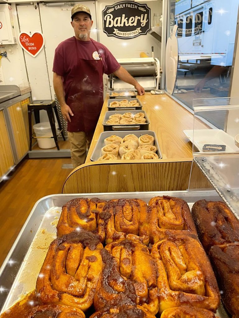Man with apron standing in kitchen with cinnamon rolls